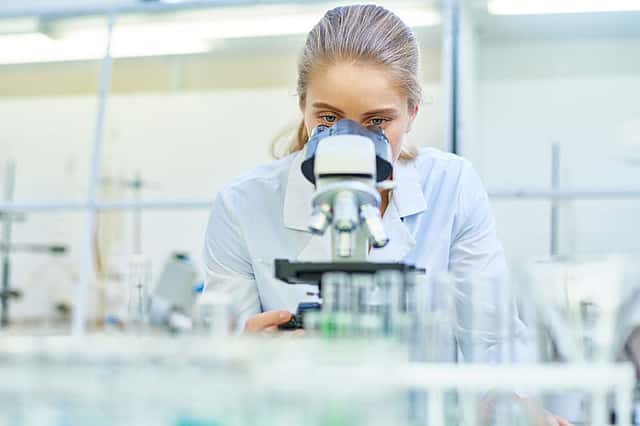 Portrait of young female scientist looking in microscope while working on medical research in science laboratory, copy space