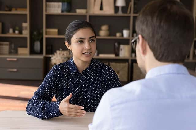Confident Indian female meet male business partner investor sit at negotiation table talk discuss commercial deal explain project benefits. Smart young lady tell about herself to hr on job interview