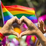 Hands making heart sign in front of rainbow flag
