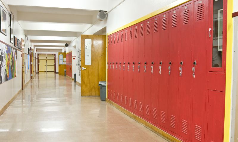 An empty highschool hallway with red lockers on the right side