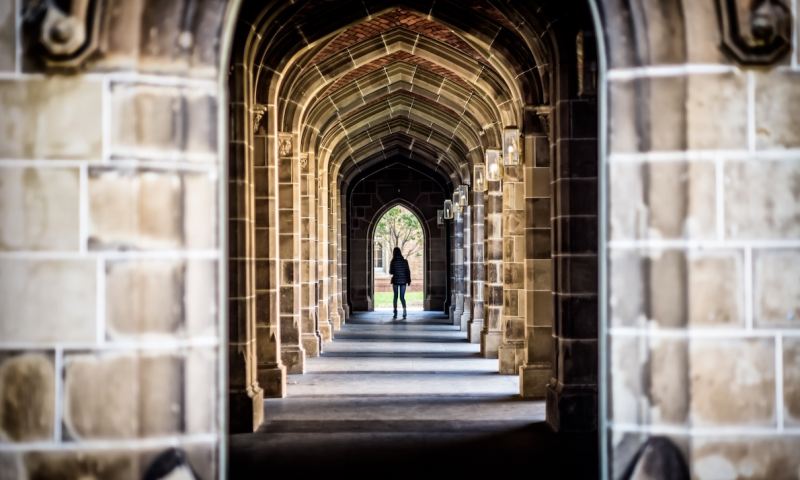 A stone arch hallway at a university with unidentified female in the distance