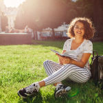 Beautiful college girl reading a book in campus park. Happy woman student learning outdoors