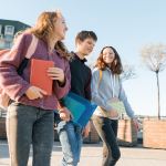 Outdoor portrait of teenage students with backpacks walking and talking. City background, golden hour