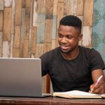 young african man studying at home using his laptop, receiving l