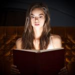 Gorgeous shocked looking young brunette woman reading book in creative lighting.