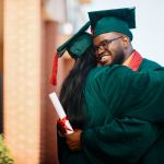 Happy black college student and his female friend hug each other while celebrating their graduation.
