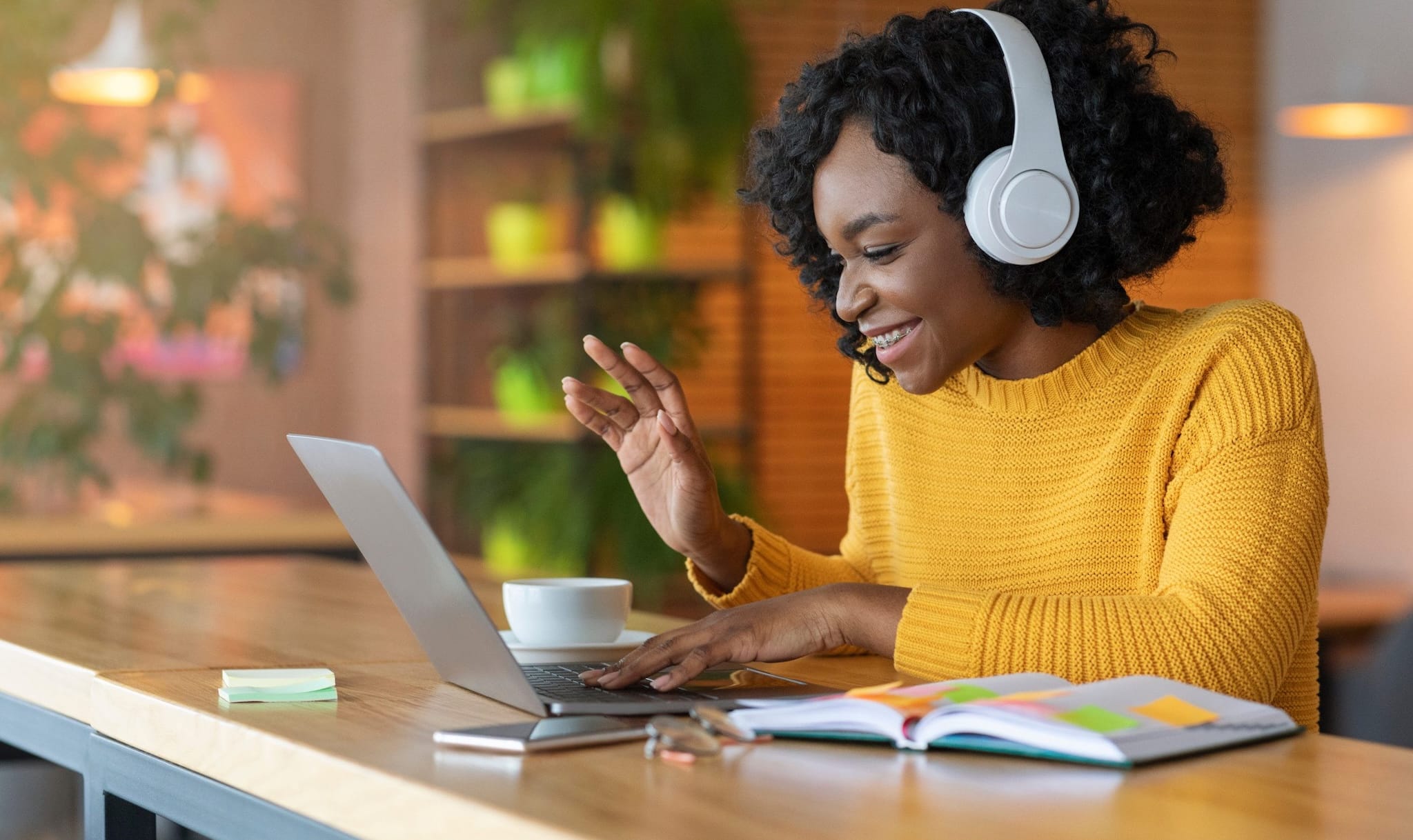 young black woman wearing headphones and waving at laptop