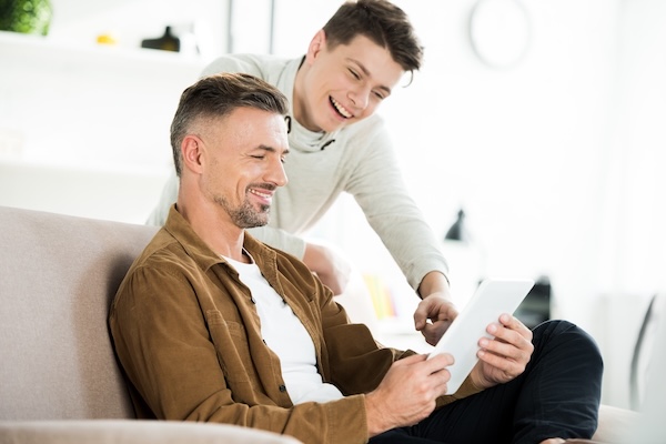 Smiling father sitting on couch while son smiles in the background.
