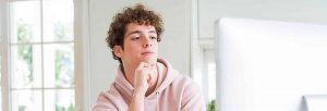 Teen student thoughtfully considers college options on computer.