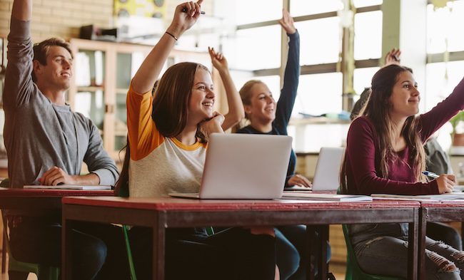 High school students rising hands in classroom.