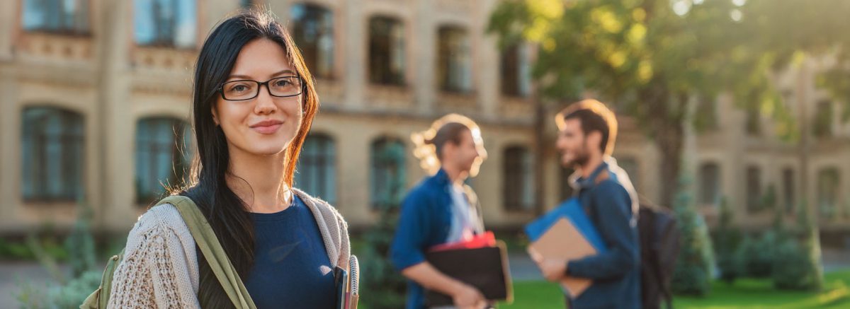 Caucasian female college student on modern campus with friends on background