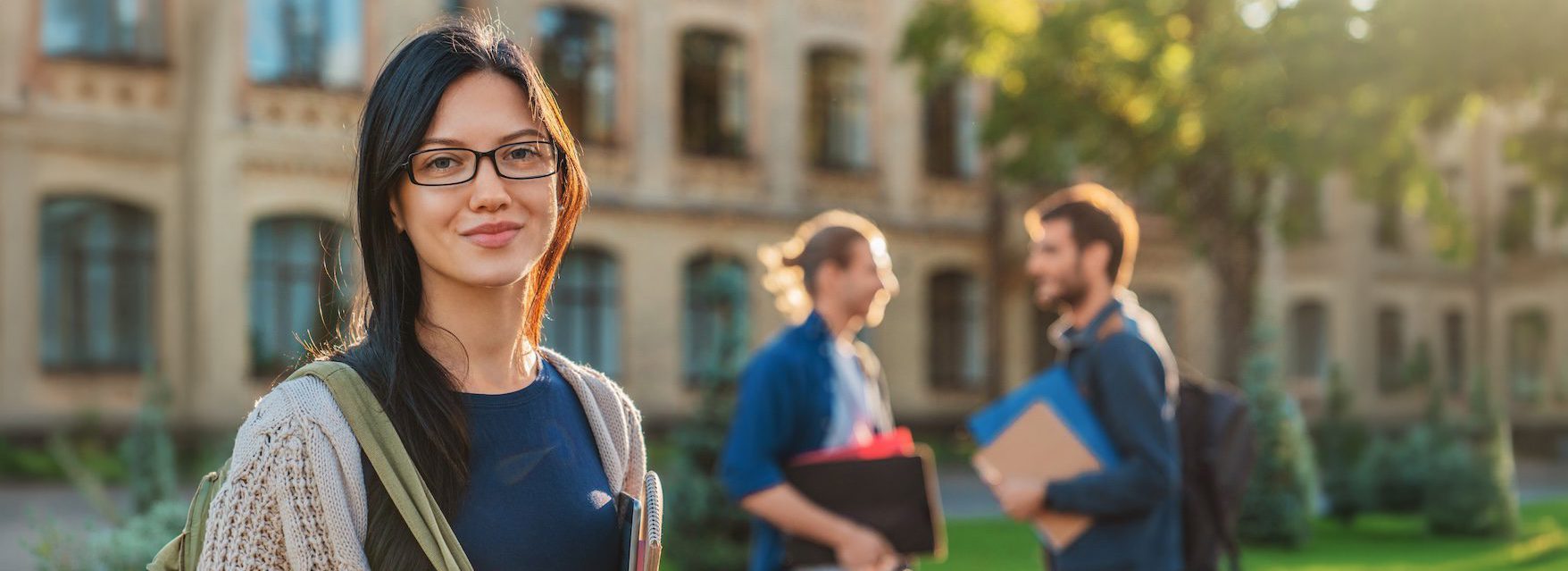 Caucasian female college student on modern campus with friends on background